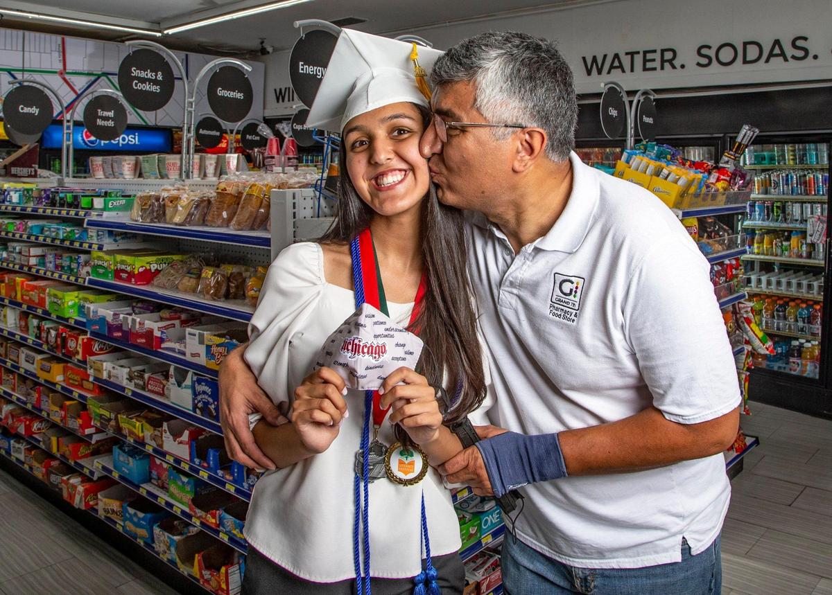 Aya Hamza, a 2021 graduate of Coral Gables Senior High School, is kissed by her father, Firas Hussain, at their convenience store, Grand 7th, in Coconut Grove. Aya is holding a face mask from the University of Chicago, where she will continue her studies.