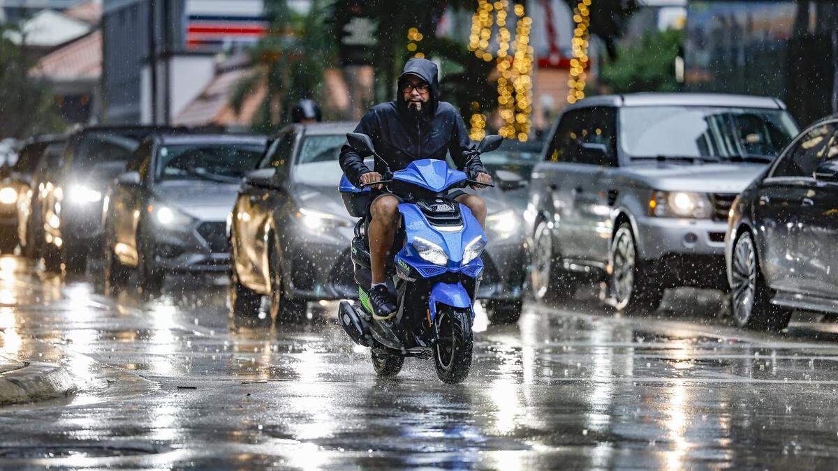 A motorcyclist dodges the rain and motorist while crossing the intersection of South Miami Avenue and Southwest Eighth Street in Miami on Wednesday, Nov. 15, 2023.