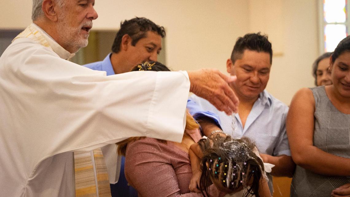 A child gets baptized by Father José Menéndez with her family on Sunday, Sept. 10, 2023, at Corpus Christi Catholic Church in Miami. Many of the children were migrants being welcomed into the church as part of an outreach effort by the Hermanos de la Calle, a organization that combats homelessness.