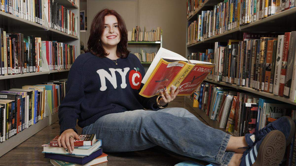 Liz Aronson poses with books on Thursday, Aug. 7, 2025, at the Miami-Dade Doral Branch Library in Doral, Fla. Aronson is doing community service with the World Literacy Foundation this summer.