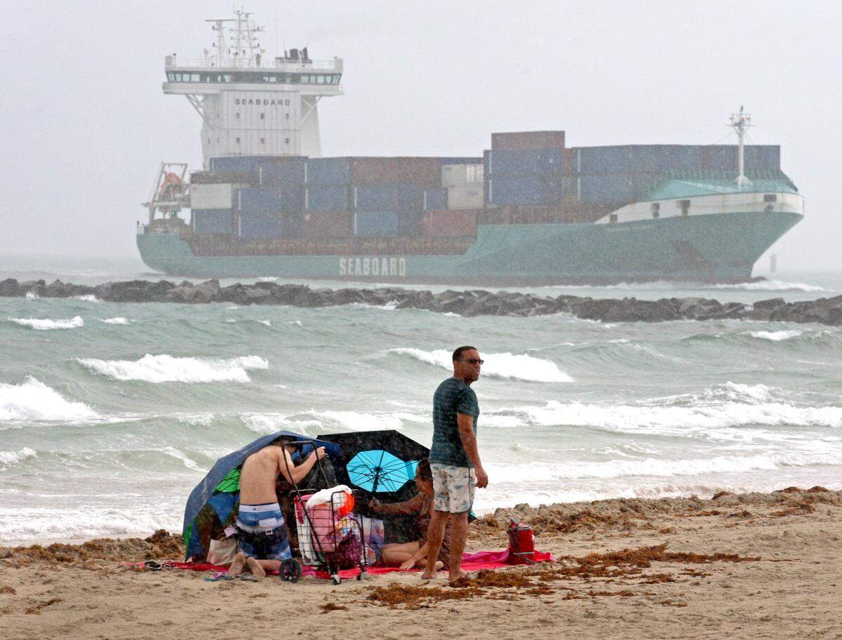Rain and wind didn’t keep these beachgoers inside as they take cover under their umbrellas as the freighter Sea Board heads toward the Port of Miami on Sunday, September 2, 2018.