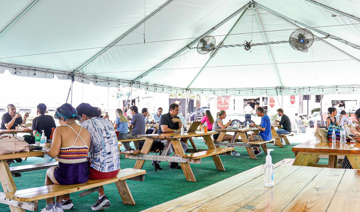 People sit at the tables inside the white tent set up at the First Miami Presbyterian Church waterfront parking lot at 609 Brickell Ave. in Miami, Florida, on Tuesday, Oct. 12, 2021.