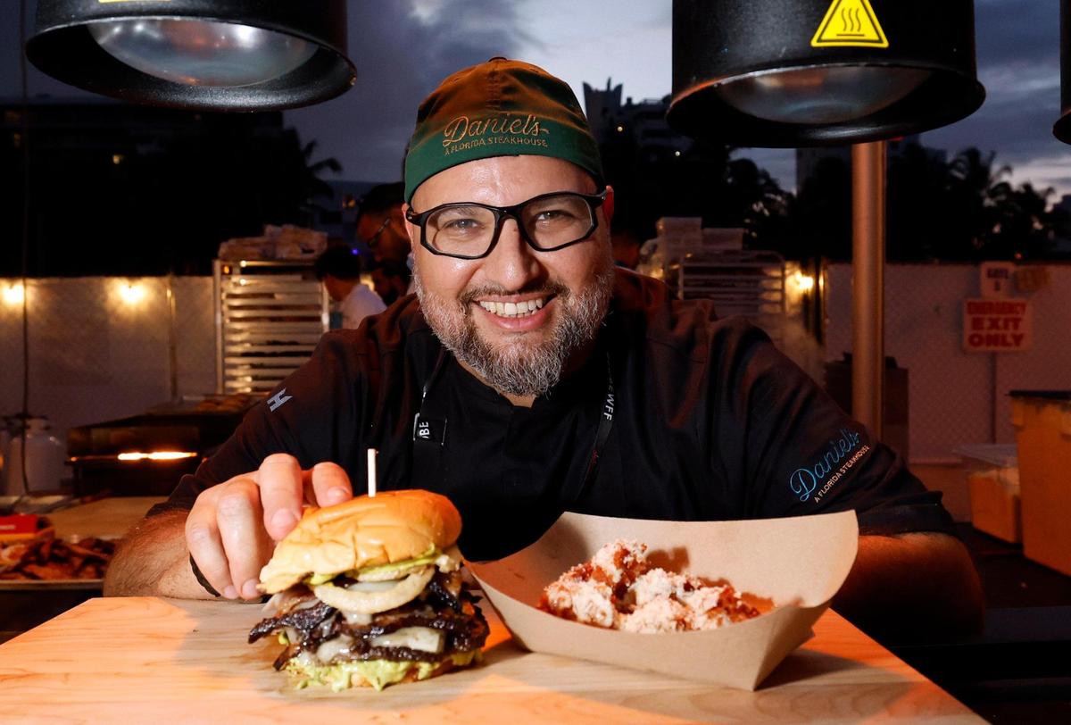 Chef Daniel Ganem from Daniel’s, A Steakhouse offers up a wagyu smash burger with double cut bacon, Florida tomme cheese and tempura onions and salsa verde mayo at the 2025 Burger Bash during the South Beach Wine & Food Festival.
