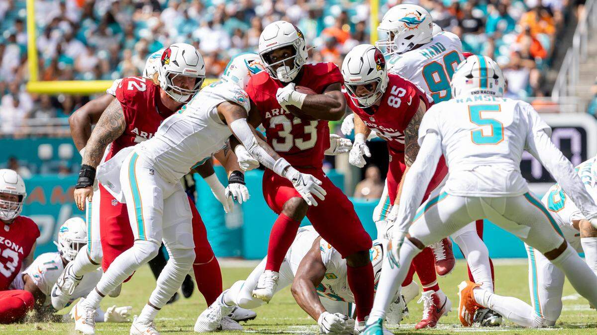 Arizona Cardinals running back Trey Benson (33) runs with the football as Miami Dolphins safety Jevon Holland (8) and Dolphins cornerback Jalen Ramsey (5) defend during the first half of an NFL game at Hard Rock Stadium on Sunday, Oct. 27, 2024, in Miami Gardens, Fla.