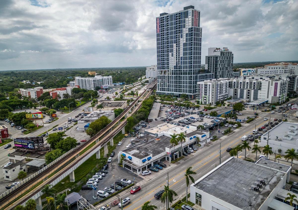 Developer Shoma Group released plans to build two 40-story apartment towers and a food hall on the Bird Road site near U.S. 1 that’s now home to a wedge-shaped portion of the Deel Volkswagen dealership, a block from the Douglas Road Metrorail station, after Miami-Dade County expanded the reach of special rapid-transit zoning rules designed to promote dense housing construction. The 37-story Cascade at Link tower, built on station property under the same rules, is visible in the background.