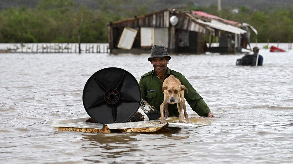 A farmer rescues his dog and some belongings from his flooded house after Hurricane Melissa passed through the town of San Miguel de Parada in Santiago de Cuba province on October 29, 2025. A powerful Hurricane Melissa made landfall in eastern Cuba on Wednesday, causing damage and flooding to homes and streets in Santiago de Cuba province, an AFP team on the ground reported. 