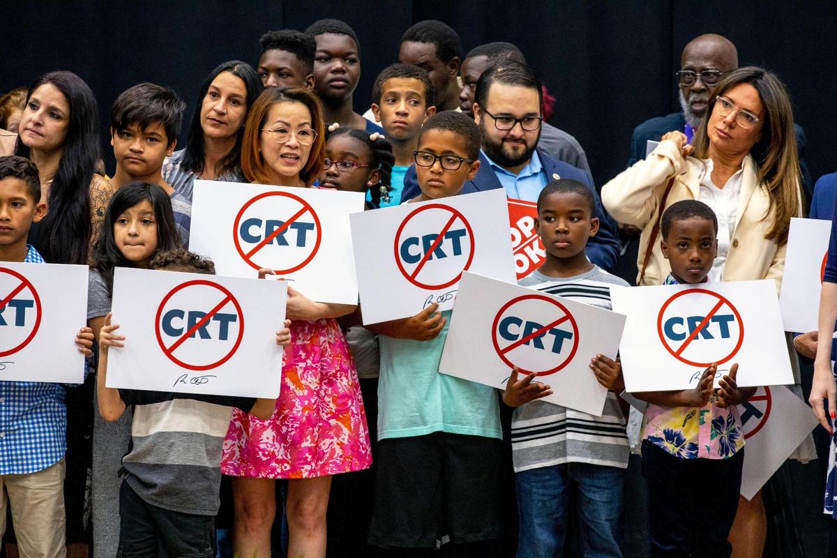 Niños que sostienen carteles contra la Teoría Crítica de la Raza se paran en el escenario junto al gobernador de la Florida, Ron DeSantis, mientras se dirige a la multitud antes de firmar públicamente el proyecto de ley HB 7, "Libertad Individual", también apodado el proyecto de ley "Stop Woke", durante una conferencia de prensa en Mater Academy Charter Middle/High School en Hialeah Gardens, la Florida, el viernes 22 de abril de 2022. DeSantis también firmó otros dos proyectos de ley, incluyendo uno relativo al proyecto de ley "Big Tech" firmado el año pasado pero dejado de lado debido a un fallo judicial, y el proyecto de ley de distritos especiales, que se relaciona con el Distrito de Mejora Reedy Creek.
