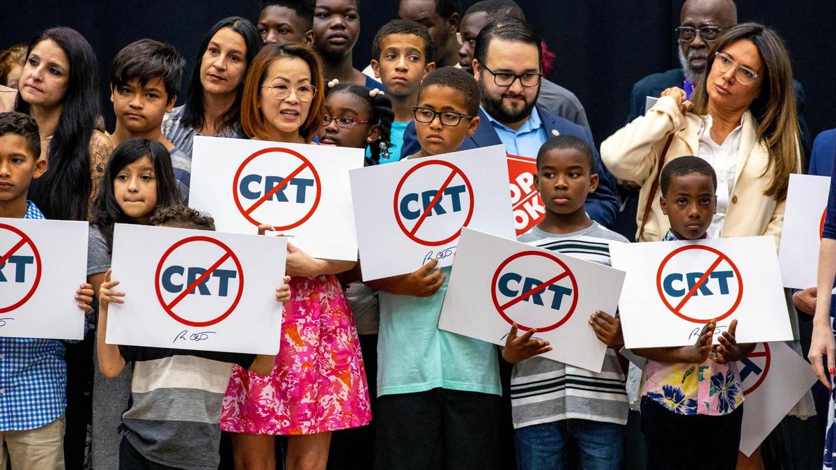 Escolares con pancartas contra el concepto de la teoría crítica de la raza en el escenario junto al gobernador Ron DeSantis mientras este se dirige a la multitud antes de firmar el proyecto de ley la HB 7 durante durante una conferencia de prensa en Mater Academy Charter Middle/High School, en Hialeah Gardens, Florida, el 22 de abril de 2022.