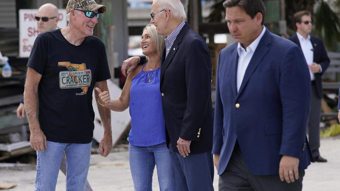 President Joe Biden talks with people impacted by Hurricane Ian as he tours the area affected by Ian on Wednesday, Oct. 5, 2022, in Fort Myers Beach, Fla. Florida Gov. Ron DeSantis walks by at right.