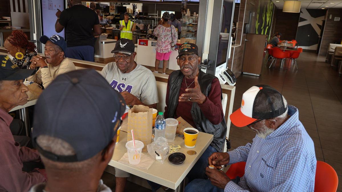El veterano de la Infantería de Marina Roosevelt Randolph (centro), conversa con otros veteranos militares negros en un McDonald's local el jueves 28 de marzo de 2024 en Miami. El grupo se reúne a diario para compartir recuerdos, historias y camaradería.