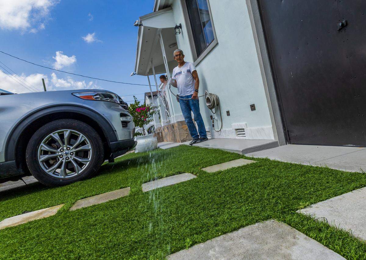 A resident named Juan Jose waters the artificial turf installed in the front of his house in the East Hialeah area, where this kind of material installation is in high demand in the area, on Tuesday, July 29, 2025.