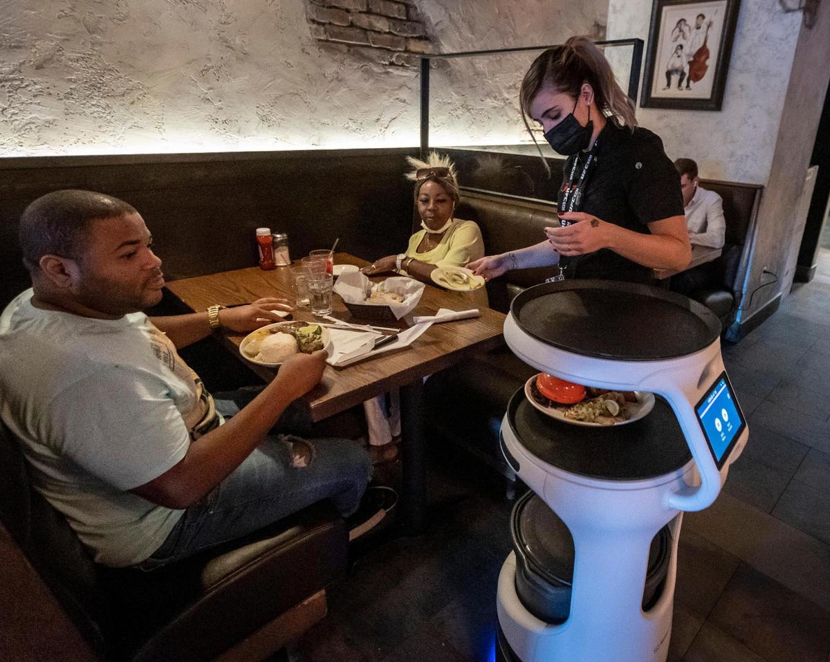 A waitress takes the food ASTRO just brought to the table from the kitchen to place on the diner’s table at Sergio’s restaurant in Kendall on May 21, 2021.