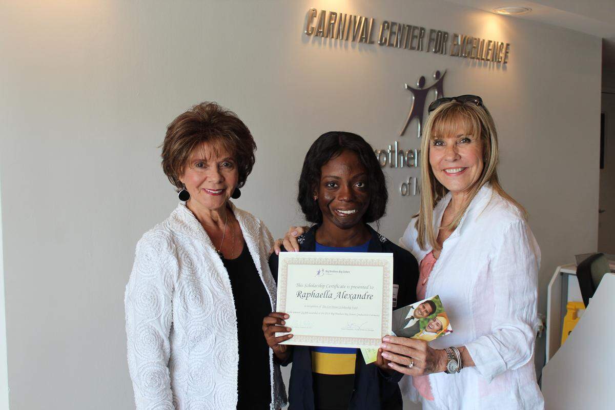 At a special small ceremony, 2018 Lori Brener Scholarship award winner Raphaella Alexandre is awarded her certificate by Miriam Salazar and Neyda Raola.