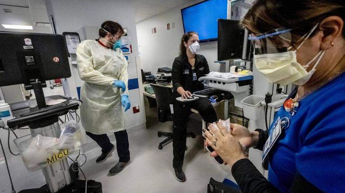 Nurse Alix Zacharski, right, sanitizes her hands as other doctors and nurses care for a patient in the Medical Intensive Care Unit for COVID-19 patients at Jackson Memorial Hospital in July.