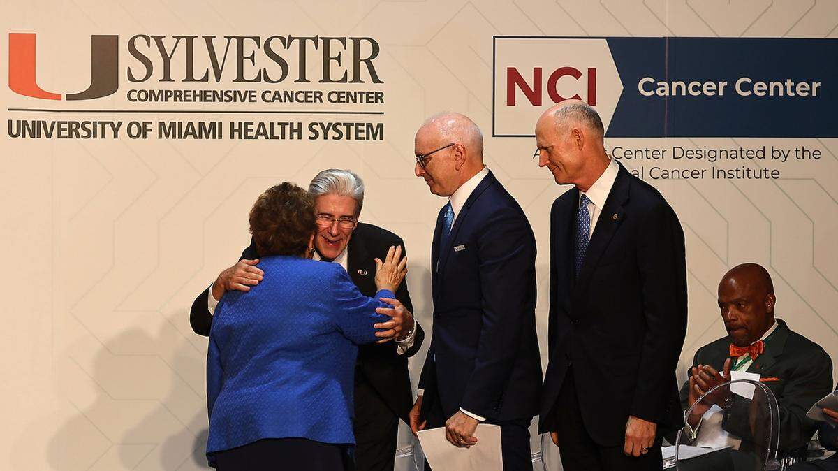 UM President Julio Frenk embraces U.S. Rep. Donna Shalala, a former University of Miami president, as Sylvester Director Stephen D. Nimer and U.S. Sen. Rick Scott share the stage.