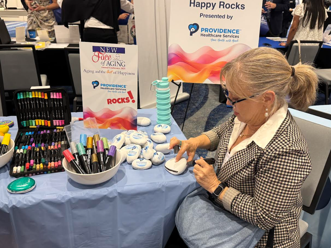 Joy Siegel, profesora de la Nova Southeastern University y miembro de la junta directiva de Alliance for Aging, pinta una piedra inspiradora en un stand de Providence Healthcare en el evento “El nuevo rostro del envejecimiento: el envejecimiento y el arte de la felicidad”, organizado por Alliance for Aging en Miami, Florida, el 2 de mayo de 2025.