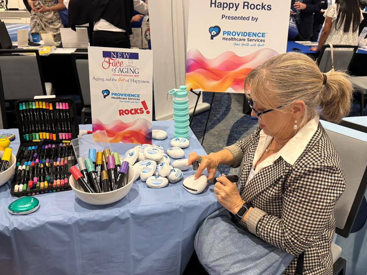 Joy Siegel, a professor at Nova Southeastern University who is also a board member of Alliance for Aging, paints an inspirational rock at a booth hosted by Providence Healthcare at the “New Face of Aging: Aging and the Art of Happiness” hosted by the Alliance for Aging in Miami, FL in May 2025.