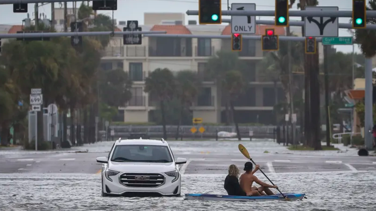 A man and woman kayak past an abandon vehicle in the intersection of Boca Ciega Drive and Pasadena Avenue Wednesday, Aug. 30, 2023 in St. Pete Beach.
