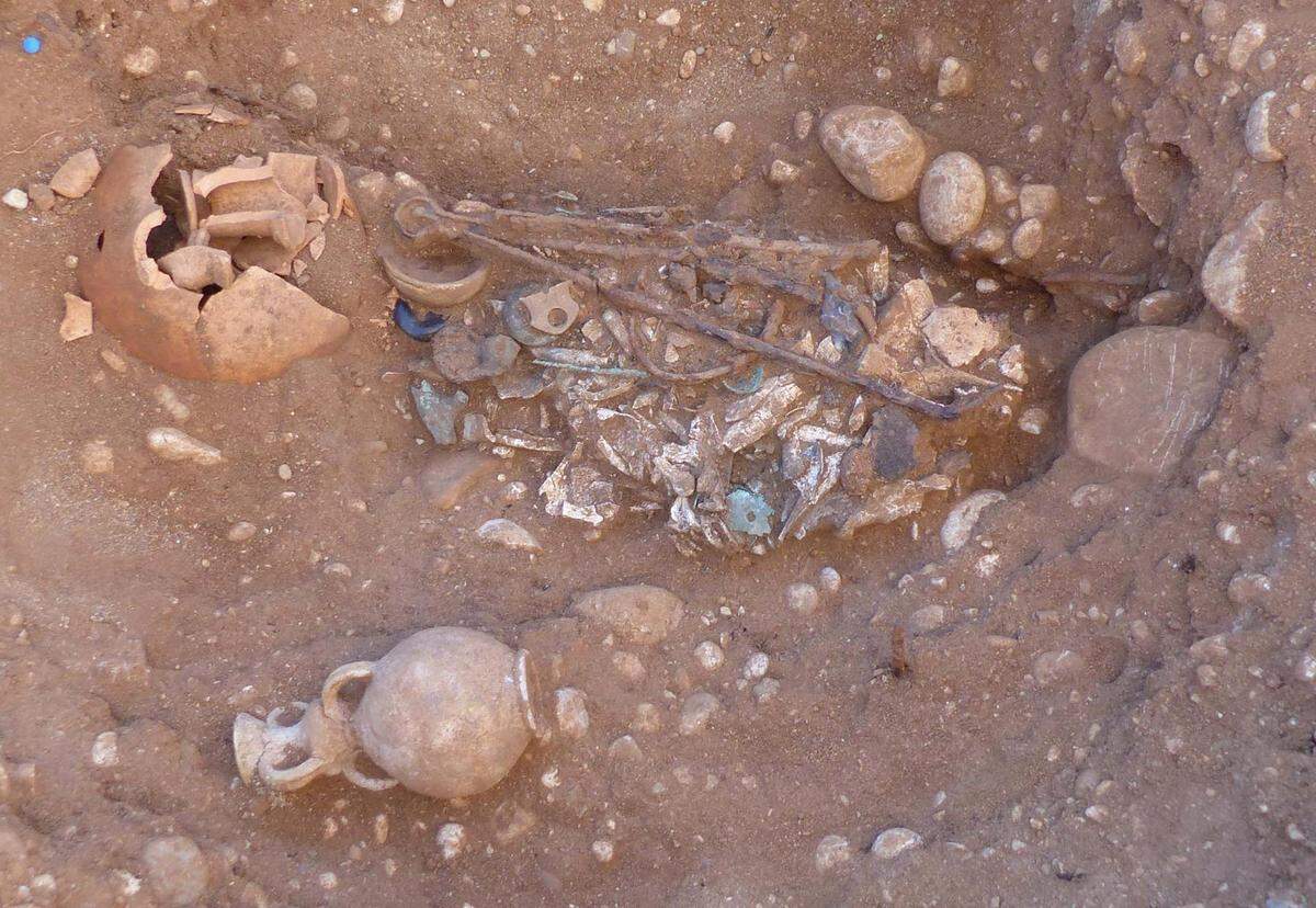 An adult buried in a wooden box with oil lamps, tongs, spoons and bracelets.
