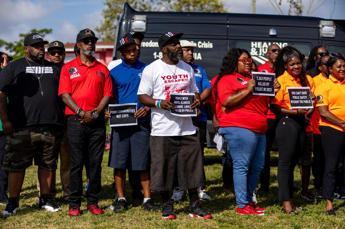 Members of The Circle of Brotherhood, Dream Defenders, Peacemakers, Touching Miami with Love and Dade County Street Response hold signs that read ‘People With Mental Illness Are More Likely To Be Killed By Police’, “1,243 People Killed By Police In 2023’ and “Fund Communities Not Cops” during a press conference held by the Healing and Justice Center across the street from the scene of a shooting at NW 58th St and NW 7th Court, in Liberty City, Florida, on Thursday, March 14, 2024. City of Miami police officers shot Donald Armstrong last week more than five times while responding to an emergency call during a mental health crisis.