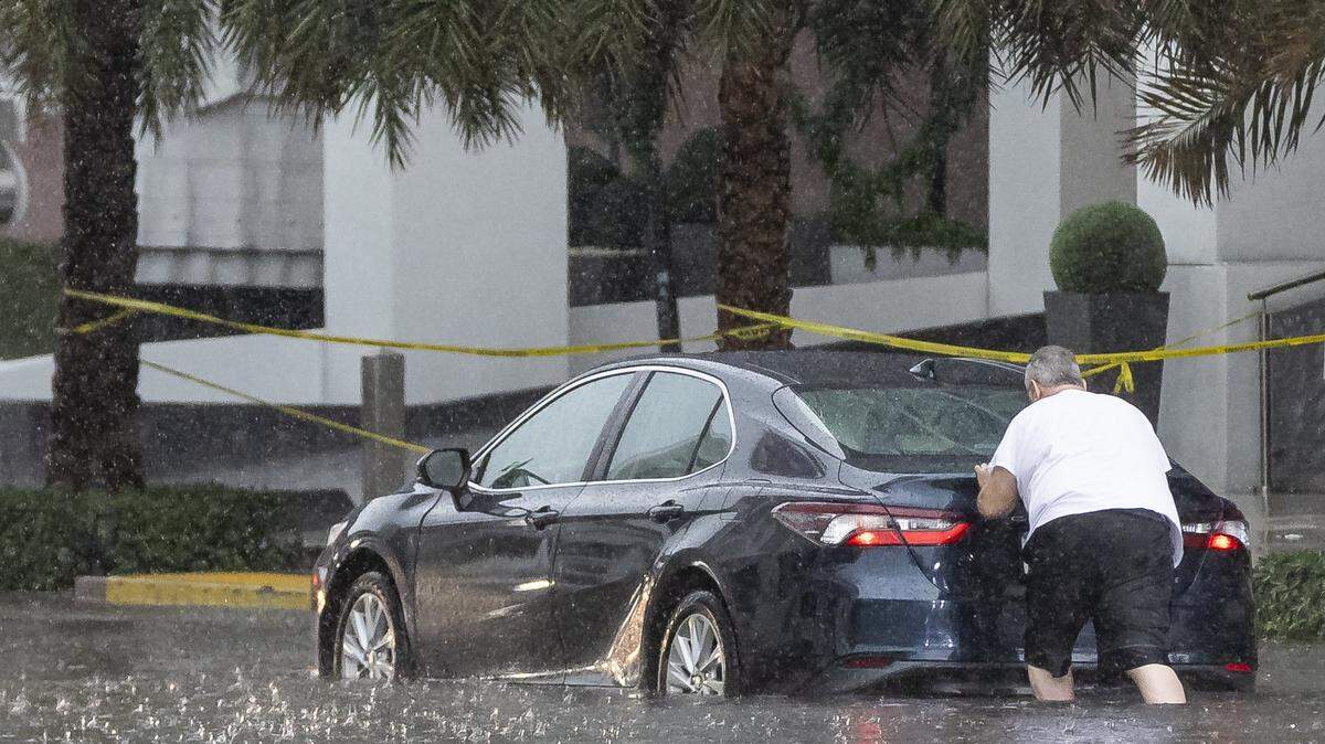 A person is seen pushing their car through a flooded portion of Northeast 11th Street in downtown Miami as lightning and heavy rain falls over the area on Monday, June 19, 2023.