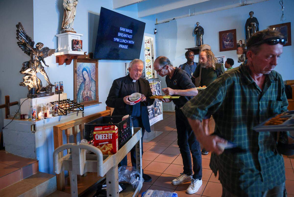 Father Bob Caudill, left, at All Saints Catholic Mission feeds the homeless as they line up for lunch despite city officials claiming it was against the rules on Monday, January 26, 2026, in Oakland Park, Florida. The city fined him $150 each day since 2016. He sued the city for religious discrimination. The trial was set to begin soon.