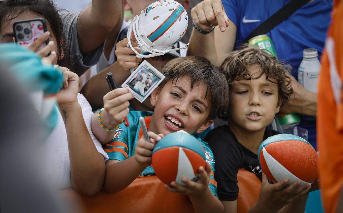 Miami Dolphins fans, Alex Baguet, 8, left and Tiago Silva, 8, right, try to get the attention of football players as they seek autographs after practice at the Miami Dolphins Training Camp in Miami Gardens, Florida.