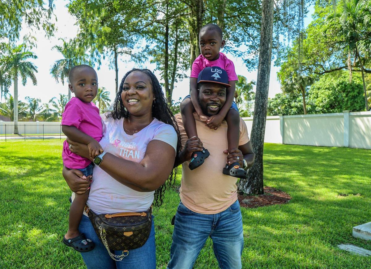 Jonise Louis sostiene en brazos a su hijo Giovanni Louis, de dos años, mientras su esposo, Milien, lleva a hombros a Brayden Louis, de cuatro años, en un parque en Lauderhill, Florida, el 7 de octubre de 2023.  Louis es sobreviviente de un cáncer de mama diagnosticado durante el embarazo. Encontró apoyo en otras mujeres embarazadas con cáncer de mama.
