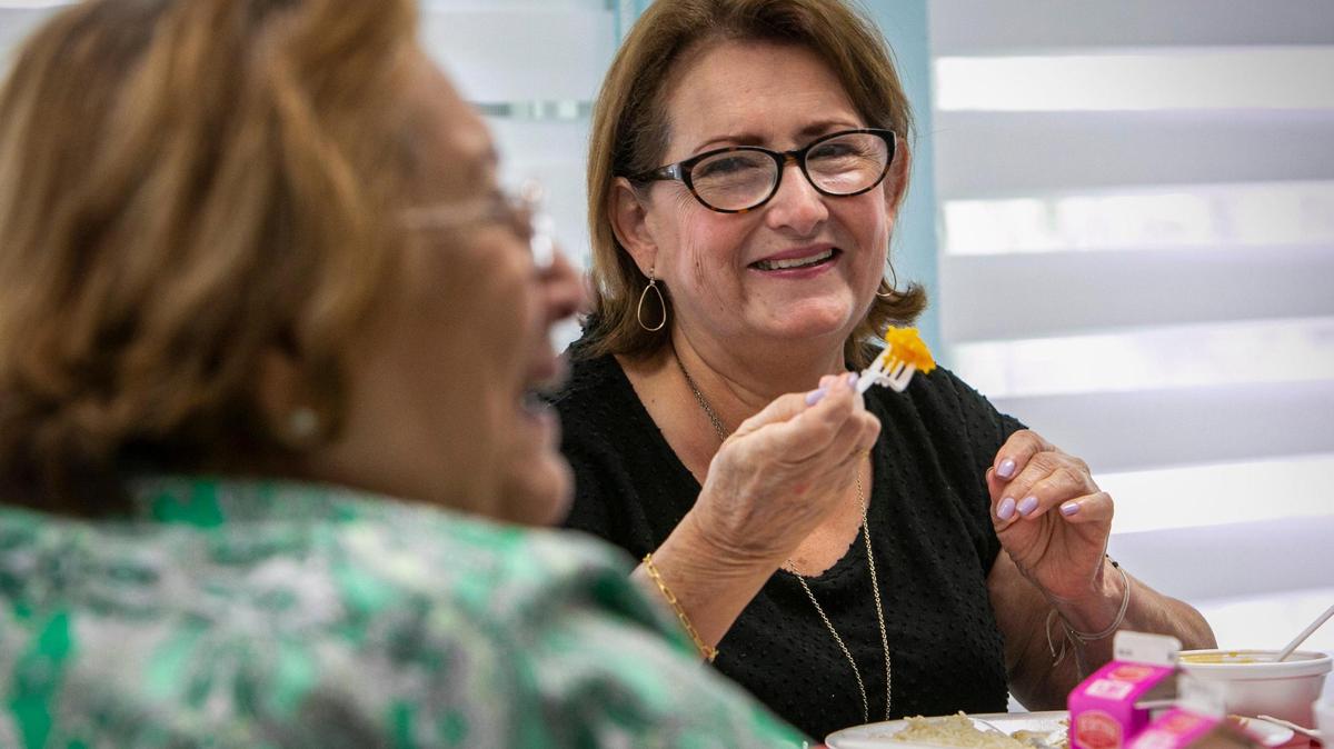 Luz Helen Albarracin, right, shares a light moment with her friend Mafalda Peña, left, in the dining room at Carroll Manor Senior Center on May 25, 2021. This is the first week of senior centers reopening their cafeterias. Many senior centers have not yet opened, but the Little Havana Activities and Nutrition Centers has reopened four, including Carroll Manor, and plans to open four more by June 14.