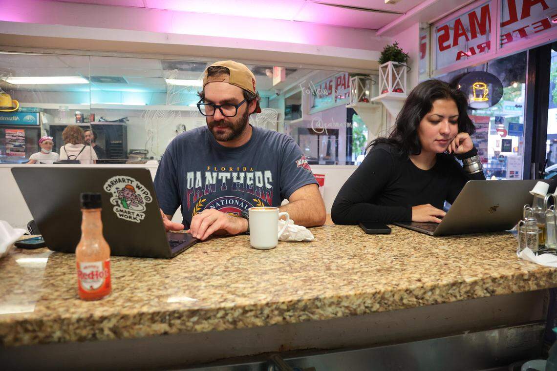 William Cormier, left, and coworker Mari Acero, right, use their laptops for work after having a meal at the bar at Las Palmas Restaurant at 209 SE First St., in downtown Miami, Florida, on Thursday, Nov. 6, 2025.