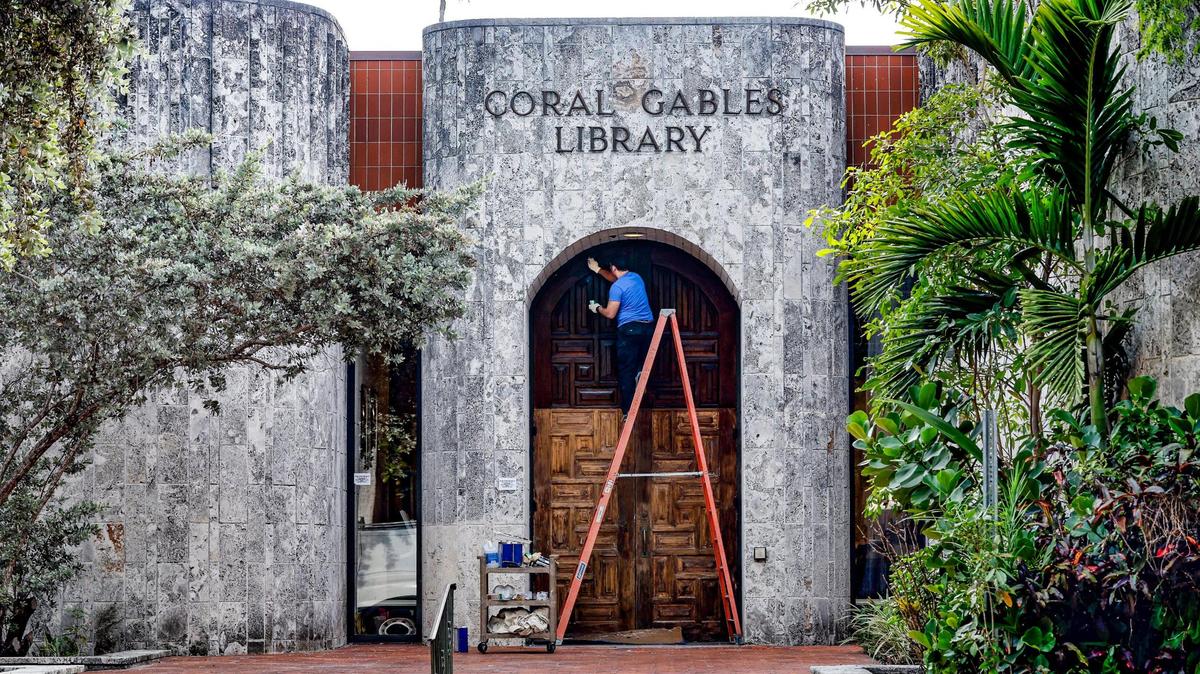 El carpintero Ceasar Aracena repasa la puerta principal de la Biblioteca de Coral Gables, que reabrirá el lunes 22 de mayo después de cerrar por reformas en 2021. La biblioteca está en 3443 Segovia Street, en Coral Gables. Imagen del martes 16 de mayo de 2023.