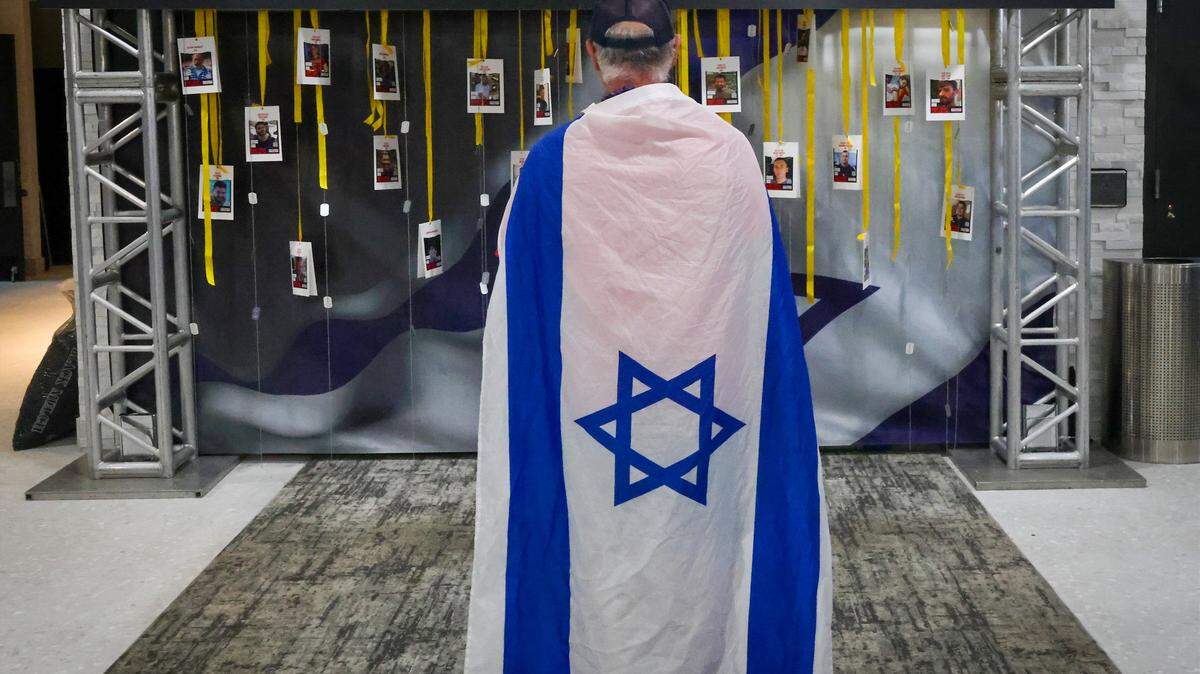 Plantation resident Bruce Goldberg, 68, center, is a member of a group called "Run For Their Lives" dedicated to walking and running on Sundays to raise awareness about the plight of Israelis who are Hamas hostages. Goldberg, draped in the flag of Israel, takes a moment to look at the installation of dog tags and photos of remaining hostages at  a Sunday event marking the second anniversary of the October 7 attack on Israel. 

