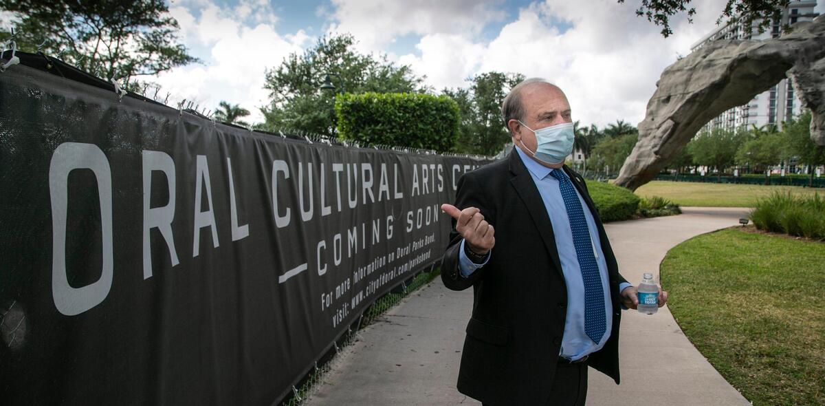 Doral, Florida, 23 de marzo de 2021 -El alcalde de Doral, Juan Carlos Bermúdez, gesticula junto al emplazamiento del Doral Cultural Arts Center. Doral ha pasado en los últimos años de ser un distrito de "logística/almacén" a un lugar donde los residentes pueden vivir, trabajar y "jugar". La ciudad está tratando de crearse una reputación como nexo del arte; una parte central de su centro ha sido recientemente rebautizada como distrito artístico. La ciudad está atrayendo eventos culturales que incluyen instalaciones de arte público y espectáculos de ballet públicos.
