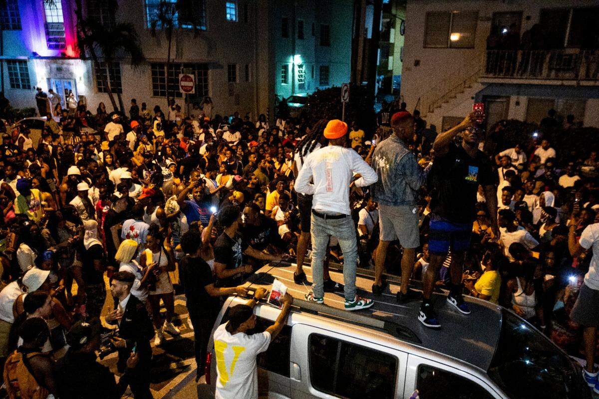 People stand on a car while a speaker blasts music an hour past curfew in Miami Beach, Florida, on Sunday, March 21, 2021. As Miami Beach police closed down Ocean Drive, droves of spring breakers moved west toward Alton Road before a few arrests broke up the crowd.