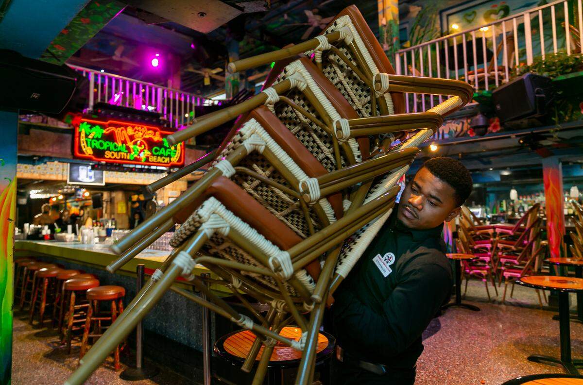 Stevenson Dieu, 26, a busser at Mango’s Tropical Cafe, stacks chairs and closes shop in Miami Beach, Florida on Friday, March 25, 2022. City officials imposed a midnight curfew and forced stores to stop selling alcohol after 6 p.m. The restrictions were set in place after two shootings in Miami Beach the weekend before caused city officials to announce a “state of emergency.”