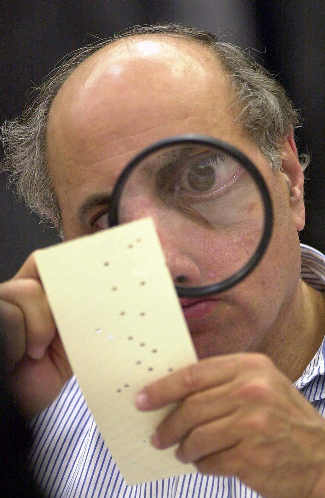 Broward County canvassing board member Judge Robert Rosenberg examines a disputed ballot in the 2000 election that became infamous for hanging chads and butterfly ballots. Following the election, Florida revised its election count laws.