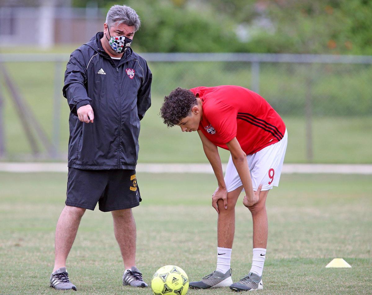 Cutler Ridge Soccer’s team coach Sebastian Fernandez talks with player Garret Gonzales in Cutler Ridge, Florida, July 10, 2020. Student athletes recondition for the fall, some wearing PPEs.