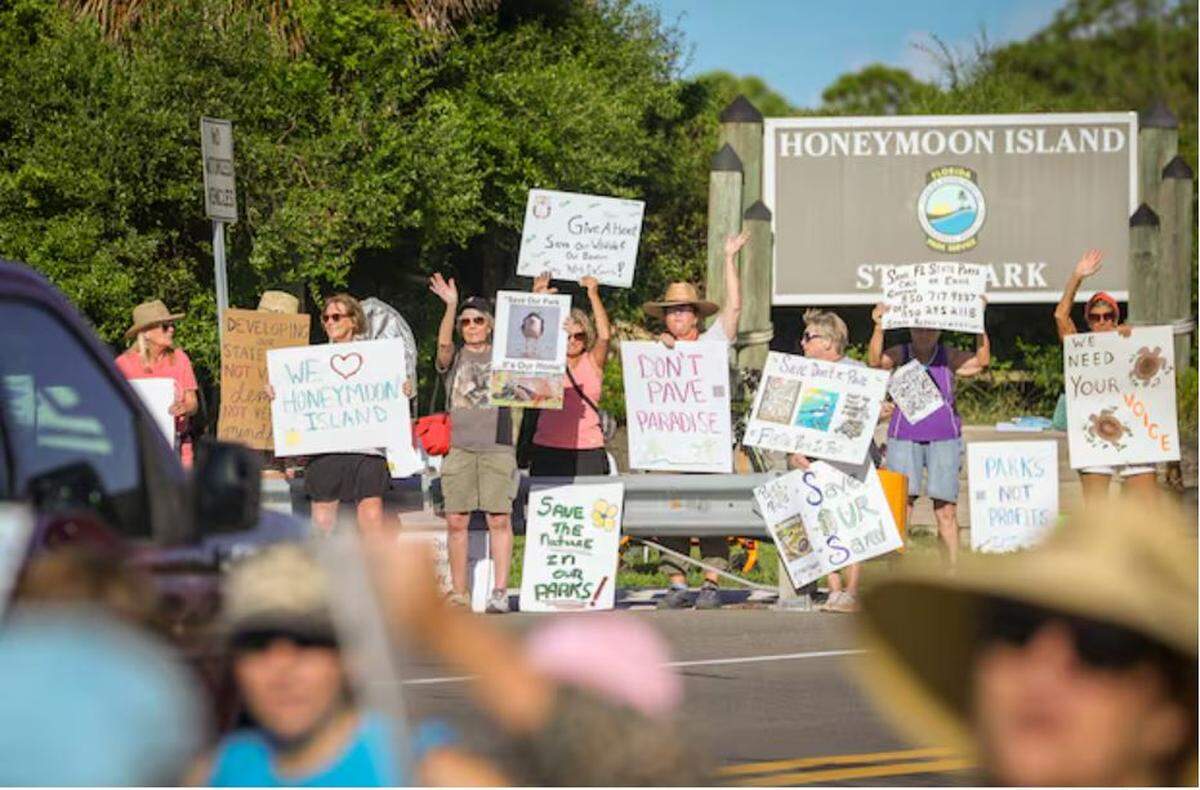 A large group waves to drivers while holding signs during a rally at the entrance to Honeymoon Island State Park Sunday in Dunedin.
