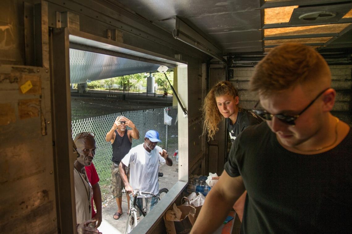 University of Miami student athletes Hannah Marwede, back, and Michael Parrot, right, give out food and water from the Second Spoon food truck in Overtown, where many homeless people stay under Interstate 395 on Saturday, July 7, 2018.