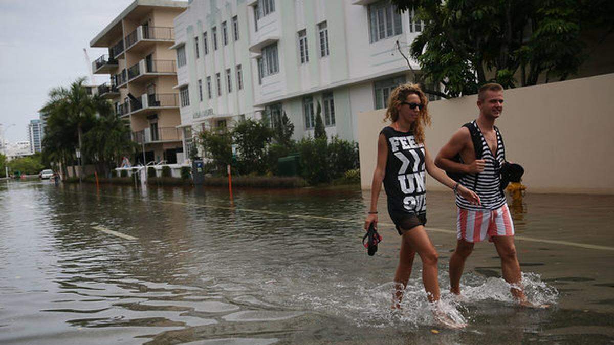 People slosh through water on a flooded street in Miami Beach.