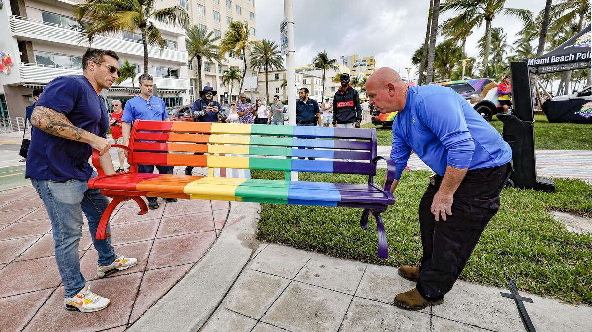 Miami BeachCommissioner Joseph Magazine and Ernesto Vasallo, left to right, carry a rainbow painted bench to Lummus Park as city officials and community members gather for the unveiling of a rebuilt LGBTQ+ crosswalk made of 3,606 colorful pavers on Friday, April 10, 2026,  The installation was created less than six months after the Florida Department of Transportation removed the original crosswalk at 12th Street and Ocean Drive in Miami Beach, Florida.