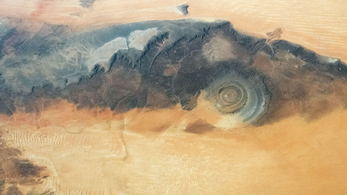 The circular formation in this photo is the Richat Structure of Mauritania, which “has captured the attention of astronauts for about as long as NASA has sent humans into orbit around Earth.”