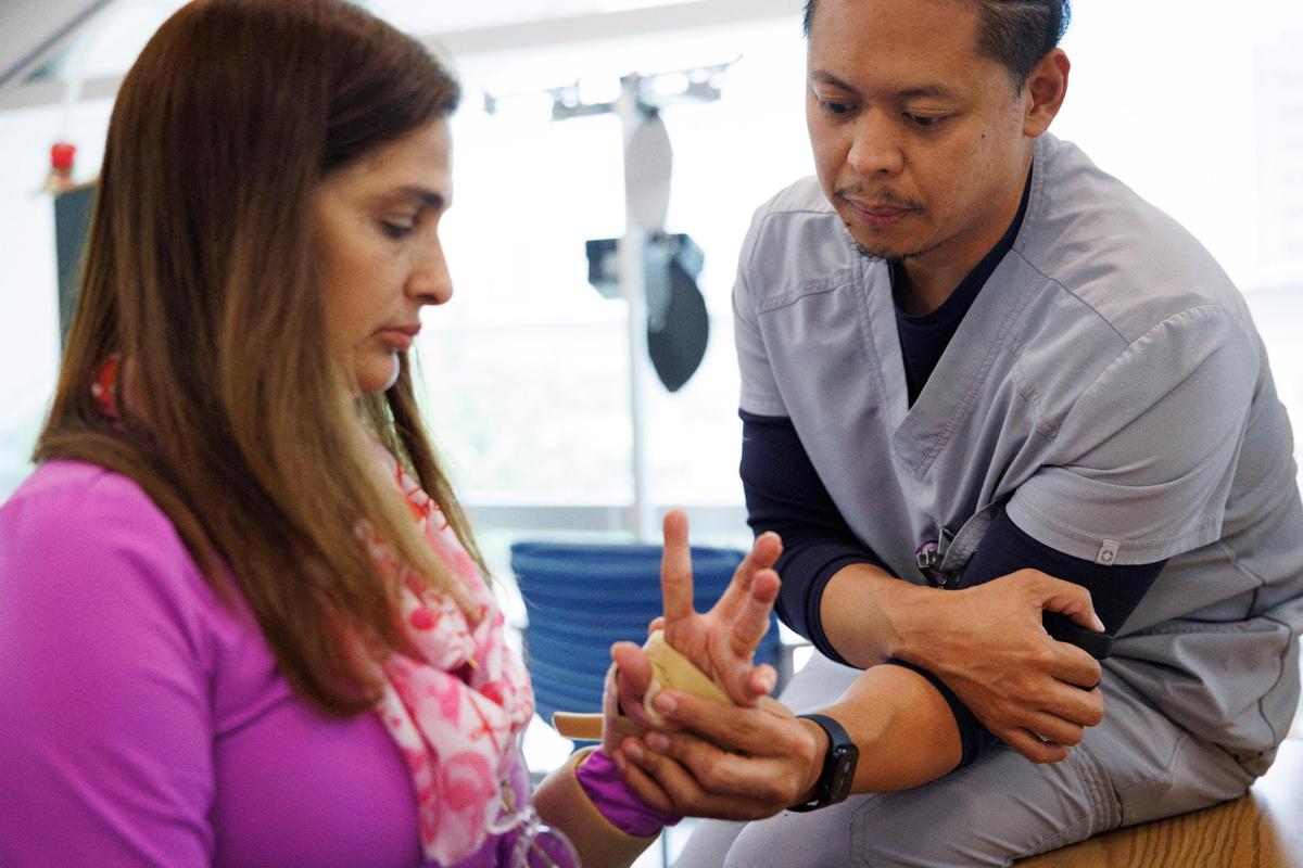 Arlet Lara, the first patient in South Florida to get an FDA-approved nerve stimulation implant, does an exercise while Neil Batungbakal, occupational therapist, activates the implant with the black trigger during her rehabilitation therapy appointment on Monday, Sept. 9, 2024, at Lynn Rehabilitation Center at Jackson Memorial Hospital. The activation works as positive reinforcement to her muscles when she completes the exercise correctly.
