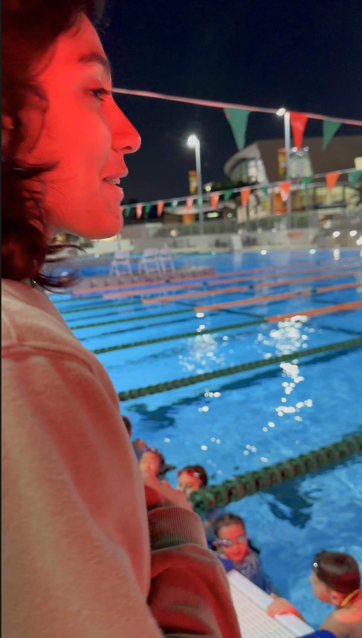 A Hurricanes Aquatics swim coach, lit by the red glow of an on-deck digital clock timer, tries to keep the age-group kids moving during a chilly night’s practice on the University of Miami pool deck on Tuesday, Jan. 7, 2025. Temperatures fell into the mid-50s. Some rising steam suggests the water was a comfy 82 degrees or so. “It’s warmer in the water than outside,” one of the kids said.