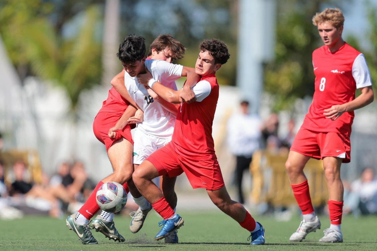 Downtown Doral midfielder Alejandro Avila (18) dribbles the ball past MAST Academy midfielder Jean De Graça (6) and midfielder Felipe Kersting (14) during the second half of a boys soccer Region 4-3A quarterfinal playoff game at MAST Academy in Miami, Florida, Tuesday, February 11, 2025.
