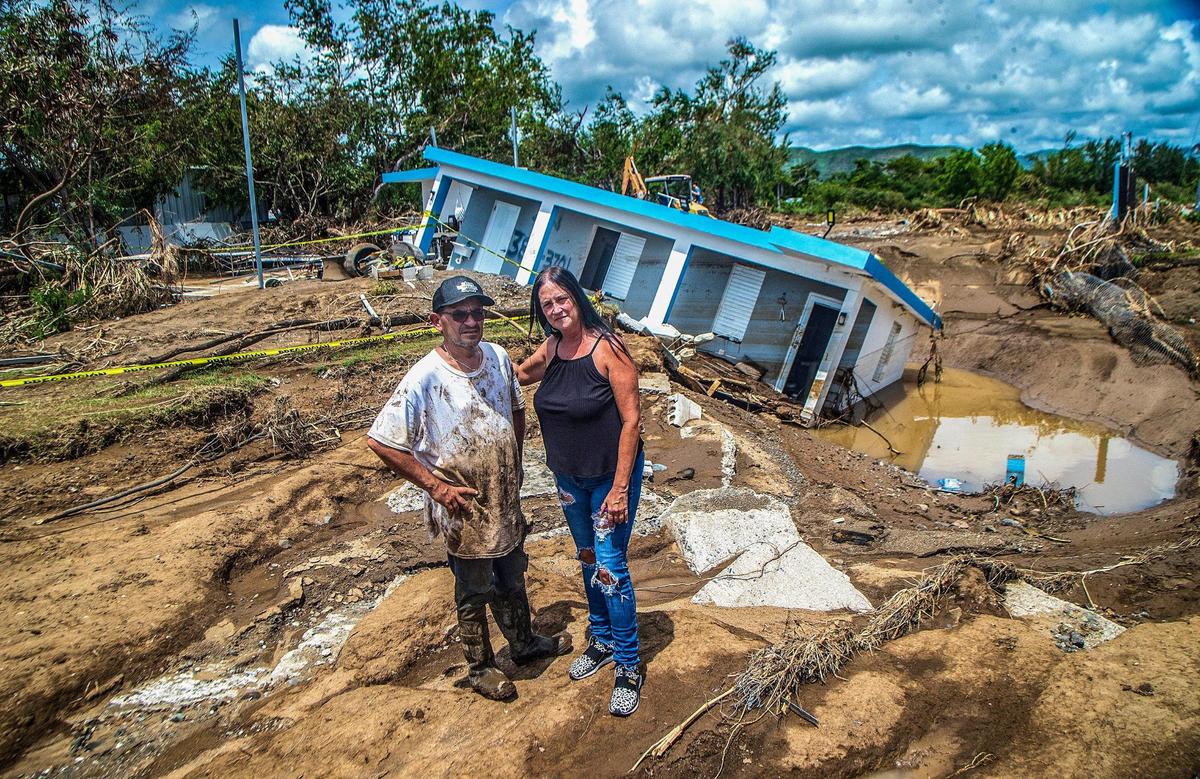 Leida Rodriguez and Javier Castellanos stand in front of their house that collapsed into a sinkhole after being flooded during Hurricane Fiona.