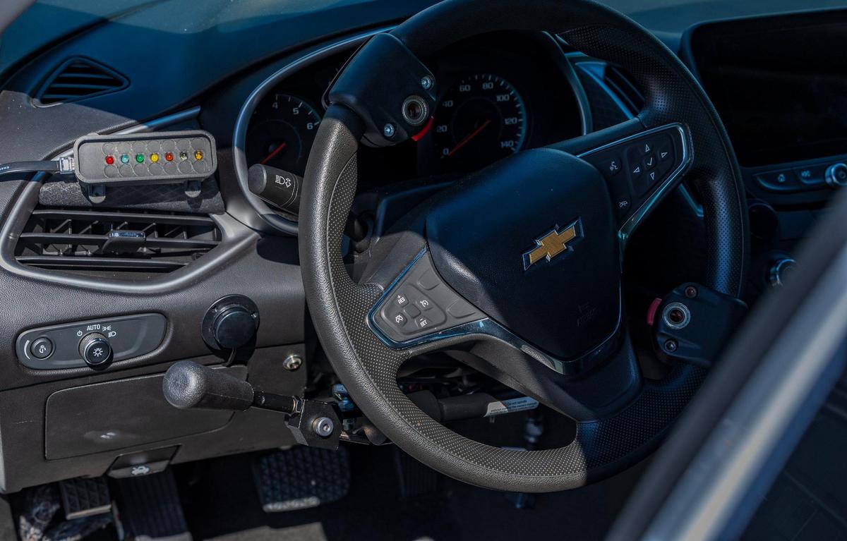A car with adaptive devices for students with disabilities features a lever to the left of the steering wheel to control the brakes and gas, and a convenient knob to control the turn signals, windshield wipers, and horn.