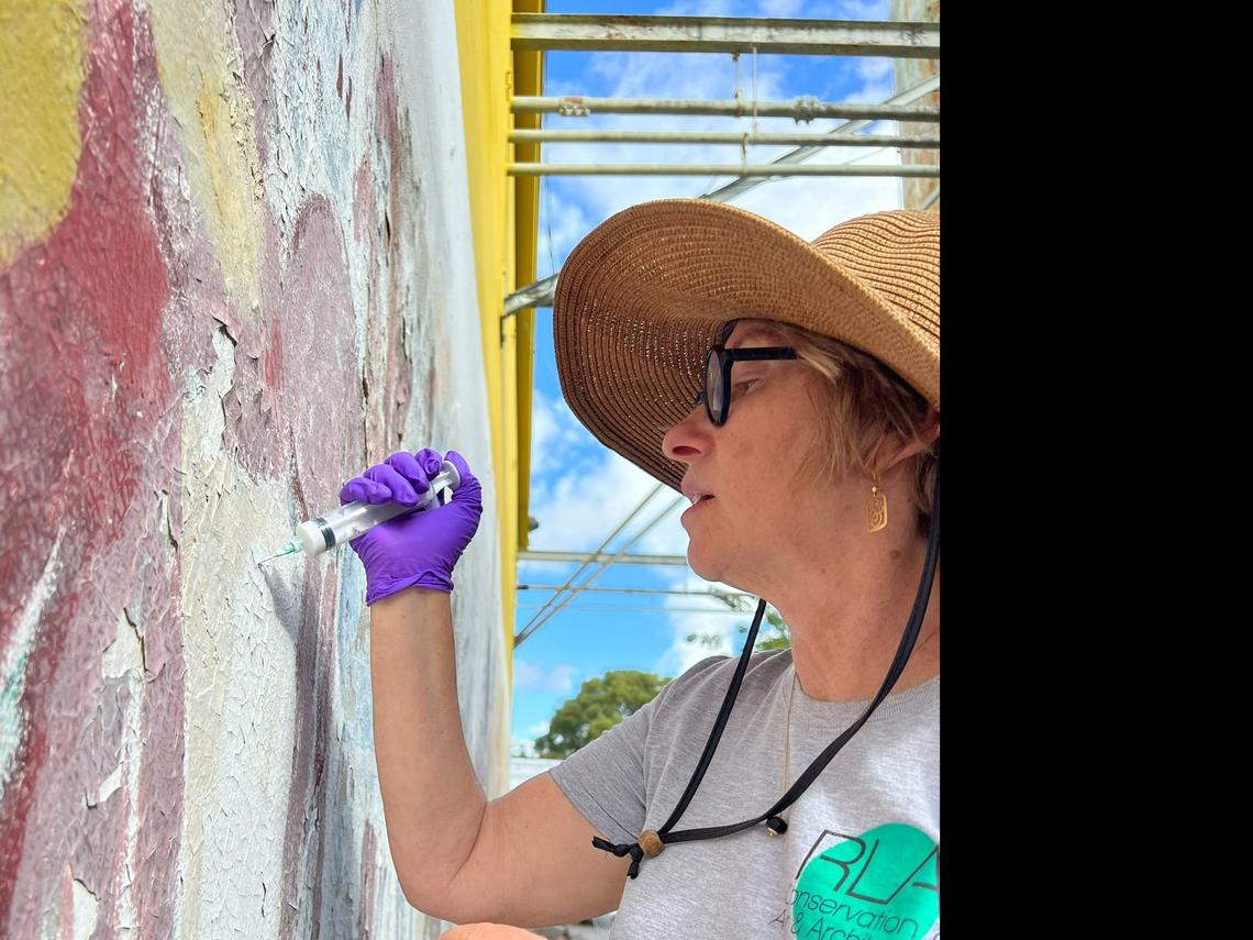 Conservator Rosa Lowinger working to preserve a mural by Miami artist Purvis Young. The mural was faded and mold was living underneath the paint.