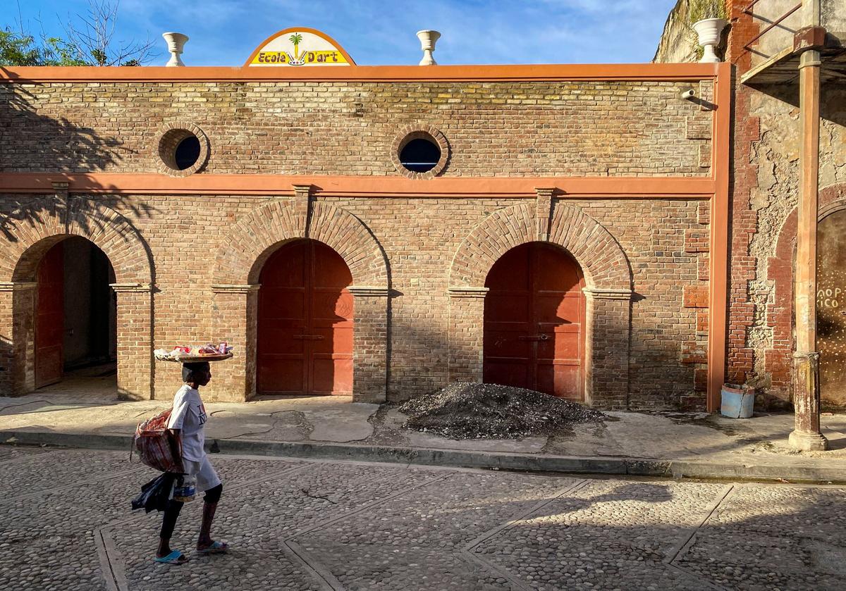 A woman walks by a building in repair in Jacmel where the tourism industry has taken a downturn, gang violence in the country being a leading reason.