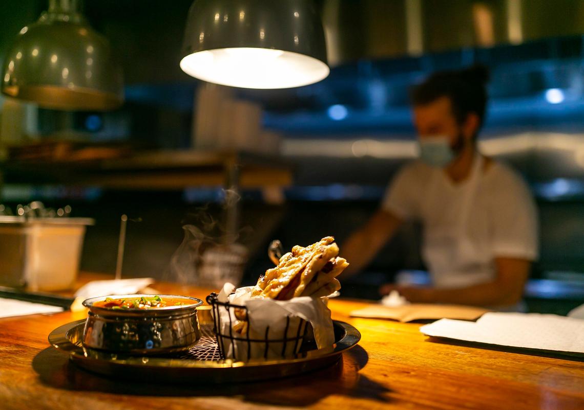 Evan Colosi, 26, a line cook at Ghee Indian Kitchen, prepares food while wearing a mask, which makes the task of working in a sweltering kitchen harder.